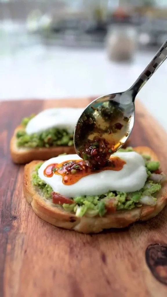 Avocado toast topped with fresh peas, garnished with herbs on a wooden table.