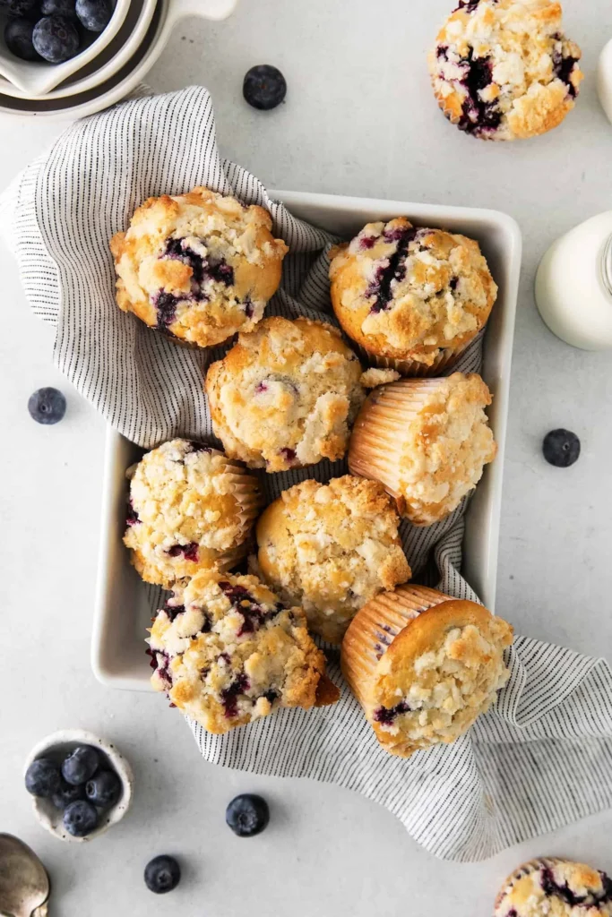 Freshly baked blueberry muffins with a crumb topping served on a plate.