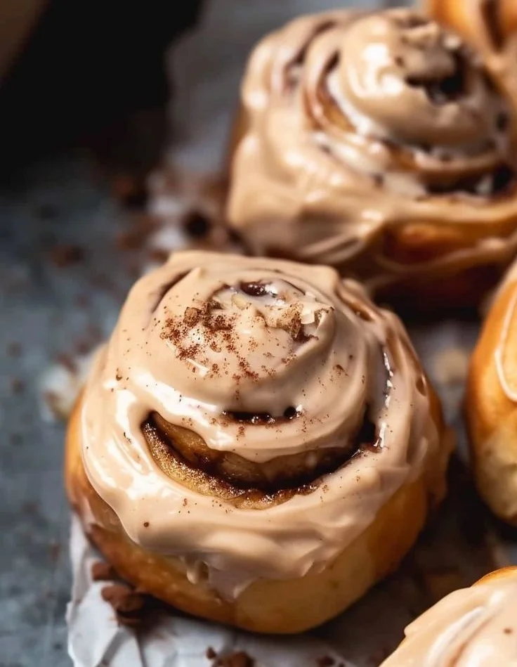 Freshly baked cinnamon rolls drizzled with light brown coffee frosting.