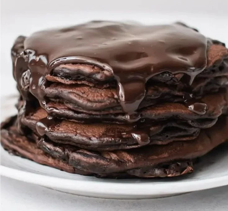 Stack of fluffy chocolate pancakes with syrup and berries on a plate