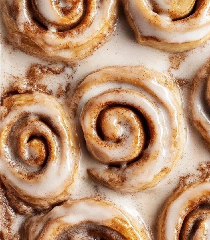 Freshly baked homemade cinnamon rolls topped with icing on a wooden table.
