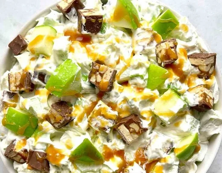Bowl of Snickers Apple Salad with apples, Snickers bars, and whipped cream