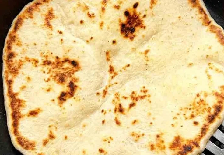 Freshly baked sourdough naan bread on a wooden board with herbs