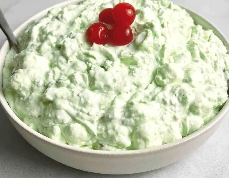A bowl of Watergate Salad with green fluff, nuts, and cherries, a classic dessert.