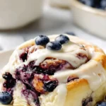 Batch of fluffy blueberry cinnamon rolls drizzled with icing on a cooling rack.