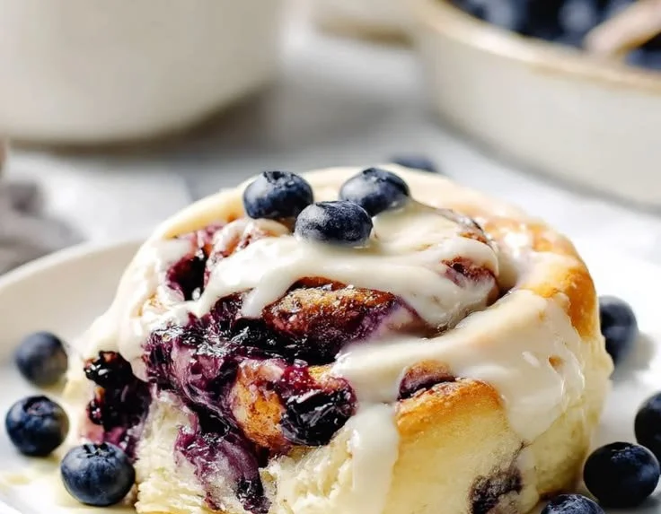 Batch of fluffy blueberry cinnamon rolls drizzled with icing on a cooling rack.