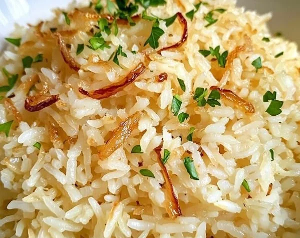 Bowl of savory jasmine rice with golden onion and butter garnished with herbs